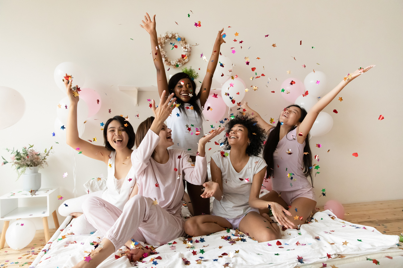 Happy young festive mixed race diverse women playing with glitter.